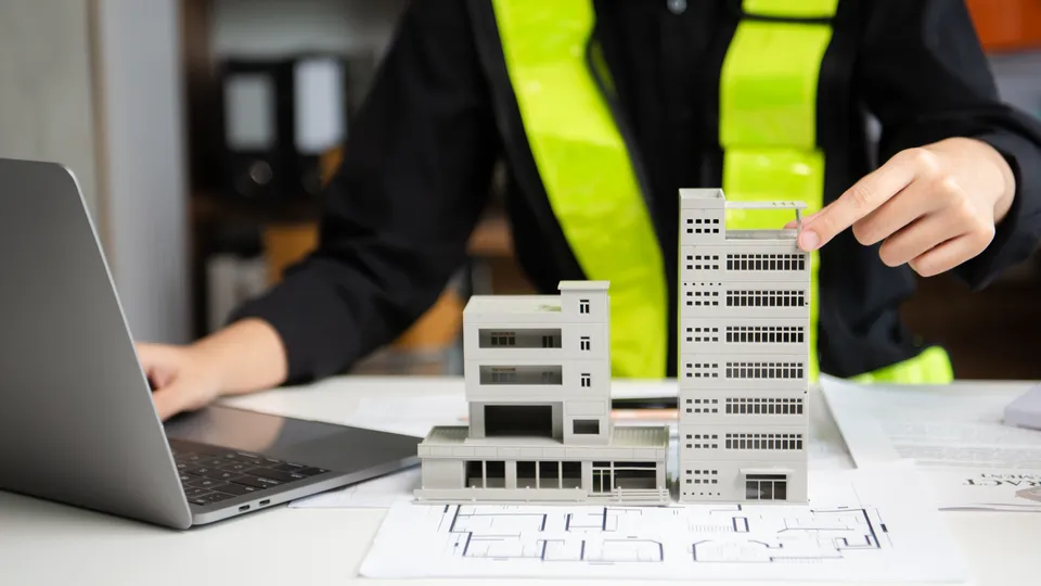 Illustrative photo: Architect working beside a scale building model.