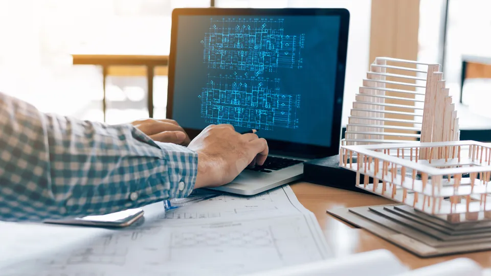 Illustrative photo: Person working on a laptop beside an architectural model.