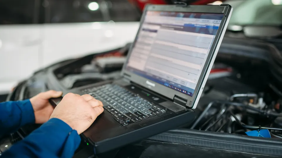 Illustrative photo: Mechanic using a laptop beside an open car engine.