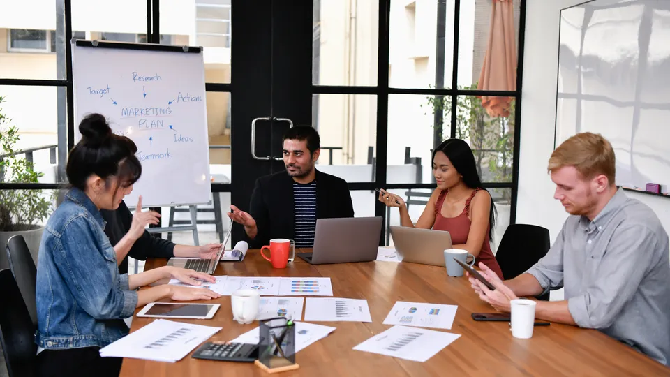 Illustrative photo: Team meeting around a table with laptops and documents.