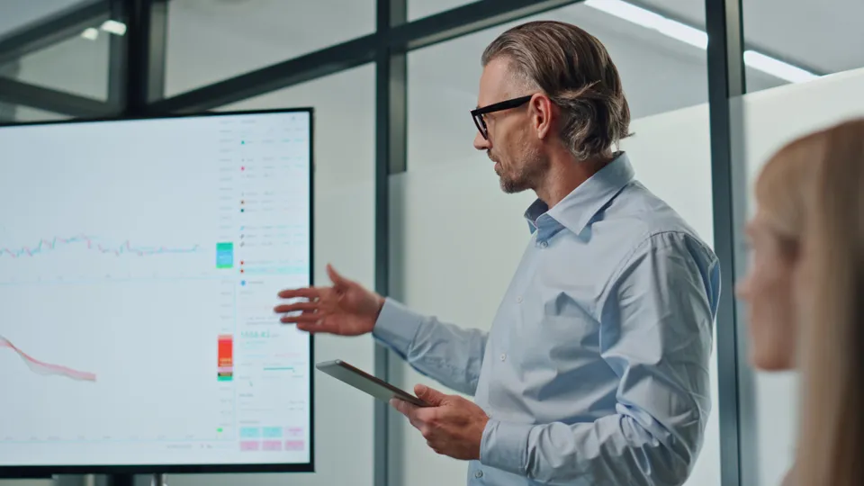 Illustrative photo: Presenter explaining charts on a large display.