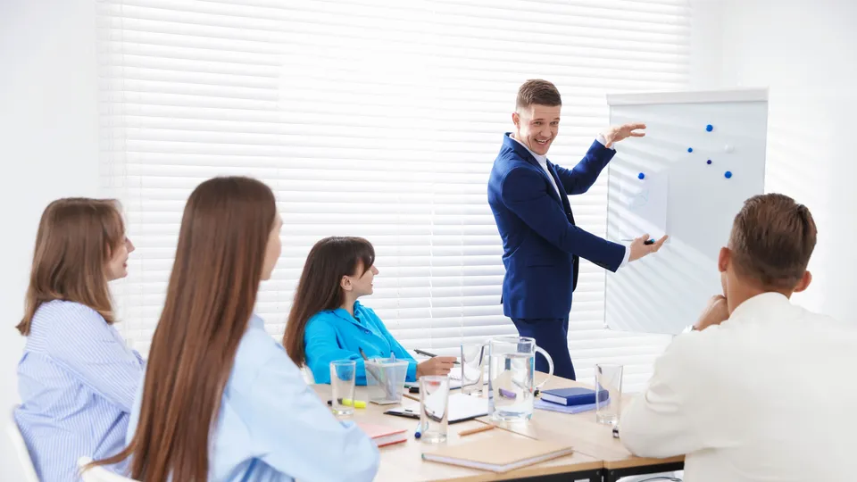 Illustrative photo: Man presenting a chart to a small group of colleagues.