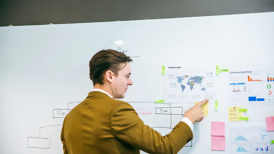 Illustrative photo: Man reviewing diagrams, charts and sticky notes on a whiteboard.
