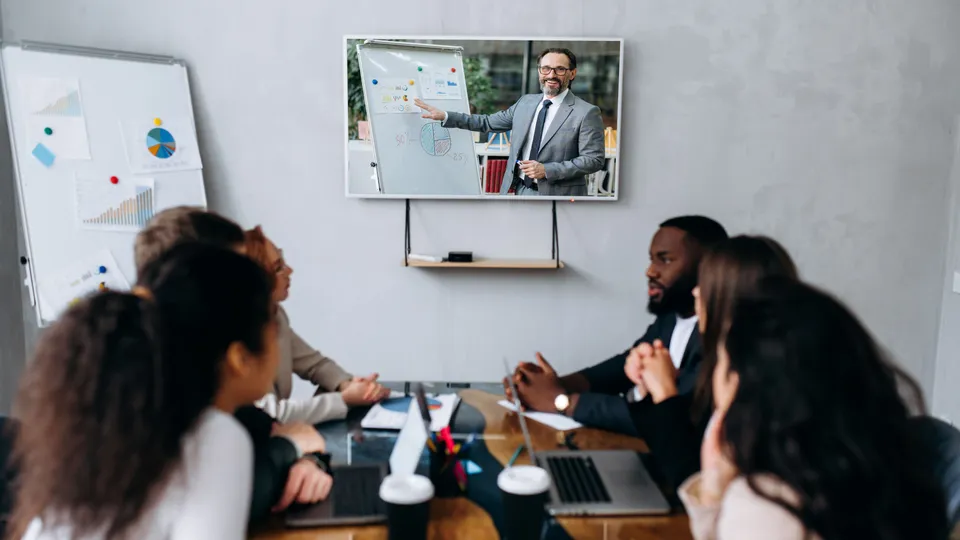 Illustrative photo: Team attending a meeting with a remote presenter on a screen.