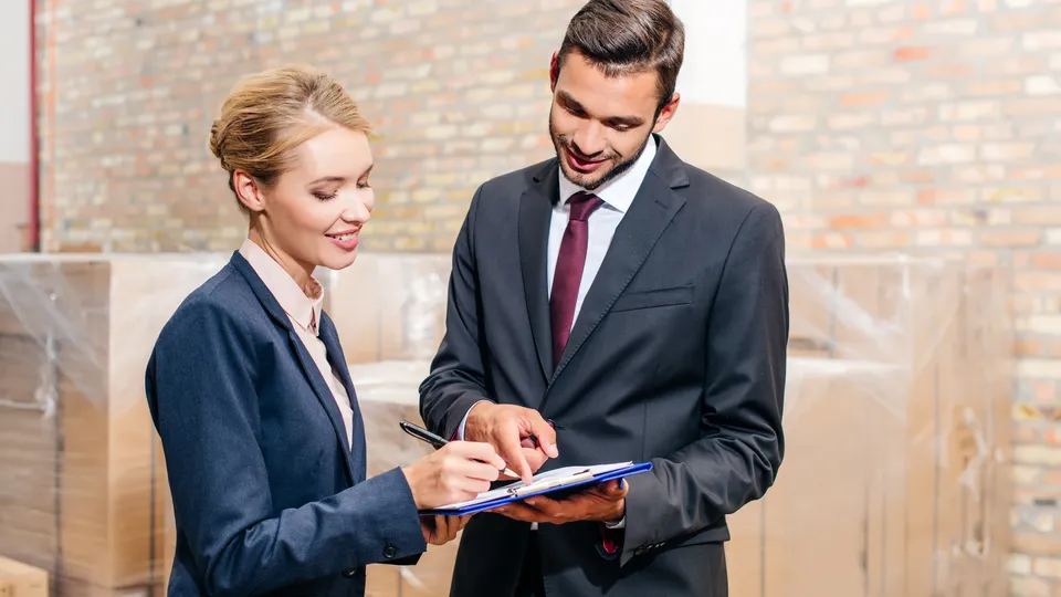 Illustrative photo: Two colleagues reviewing paperwork in a warehouse.