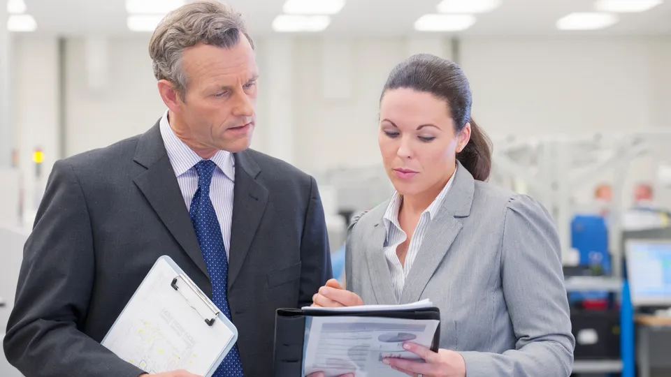Illustrative photo: Two professionals reviewing documents in an industrial workspace.