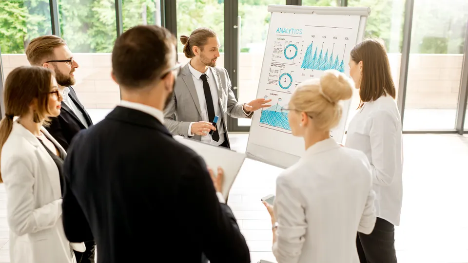Illustrative photo: Business team discussing charts on a flip chart.