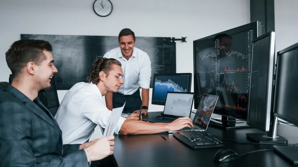 Illustrative photo: Colleagues reviewing charts on several computer screens.