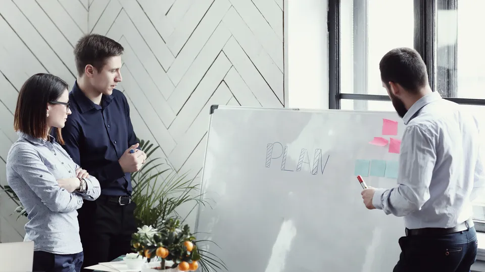Illustrative photo: Three colleagues reviewing a project plan on a board.