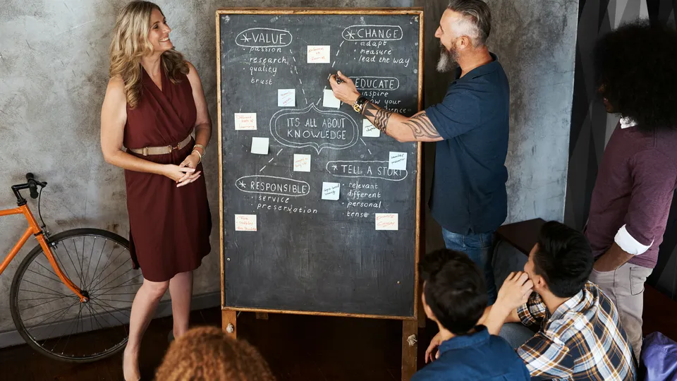 Illustrative photo: Colleagues discussing a project diagram on a chalkboard.
