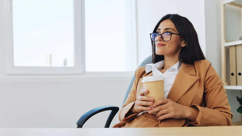 Illustrative photo: Woman holding a coffee cup while taking a break at her desk.