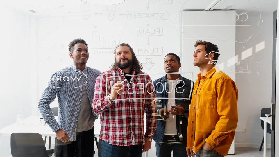Illustrative photo: Team brainstorming at a glass writing board.