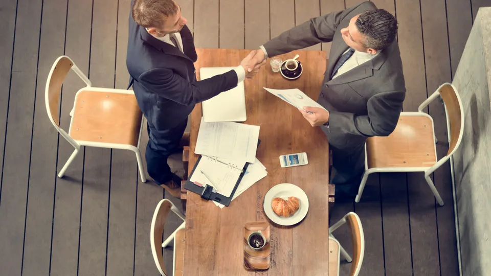 Illustrative photo: Two professionals shaking hands across a meeting table.