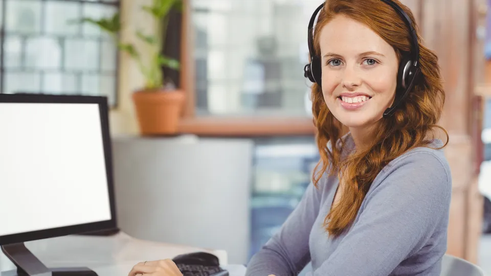 Illustrative photo: Customer support worker wearing a headset at a computer.