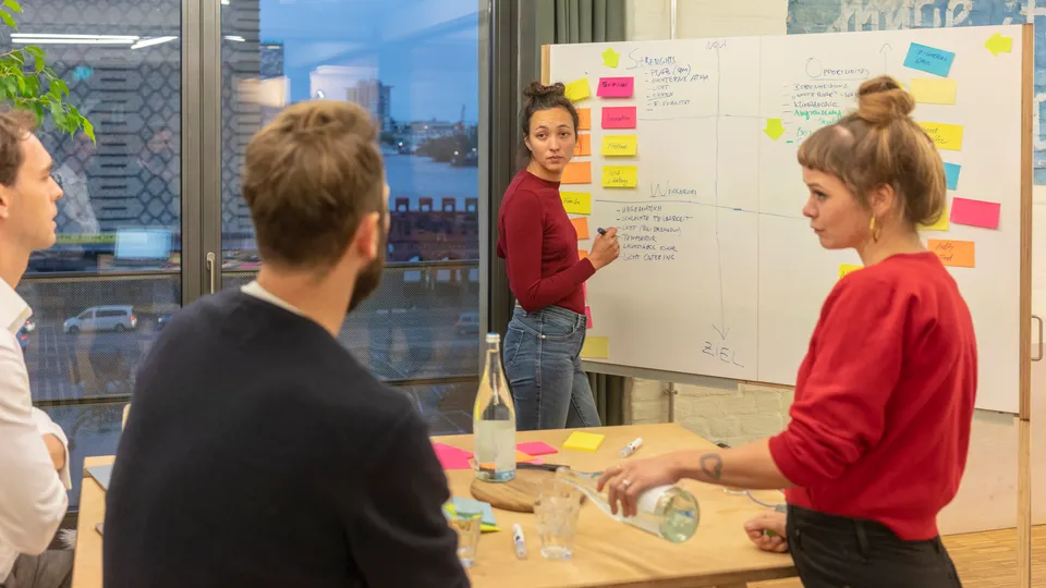 Illustrative photo: Workshop participants discussing a board covered with notes.