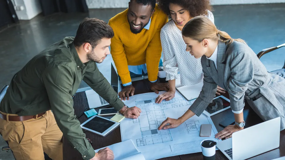 Illustrative photo: Team reviewing large architectural plans around a table.