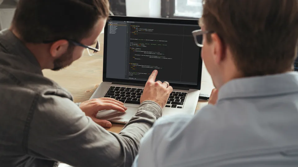Illustrative photo: Two developers reviewing code on a monitor.