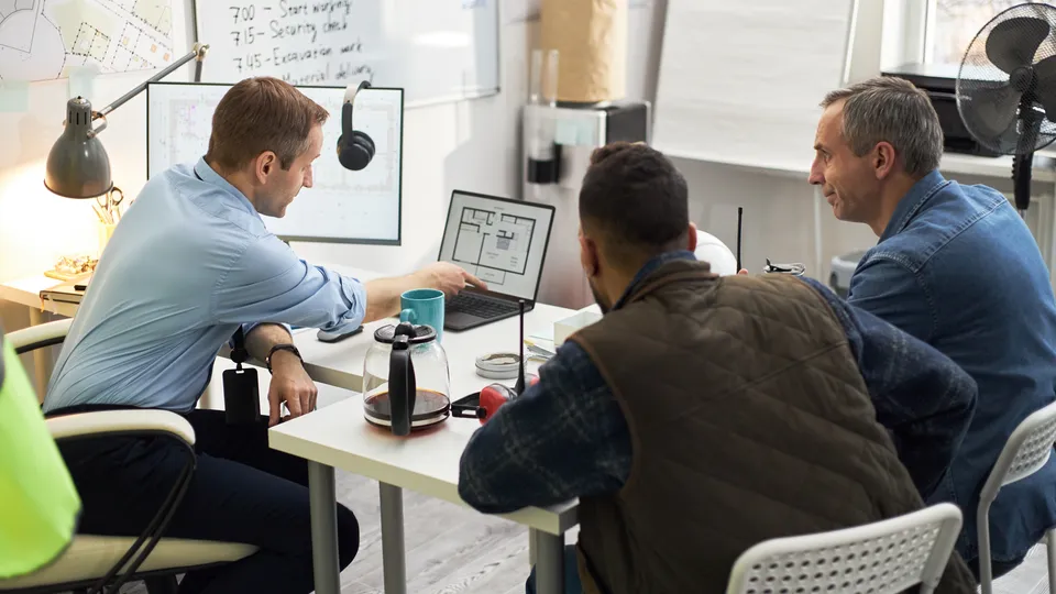 Illustrative photo: Colleagues discussing a building floor plan on a monitor.