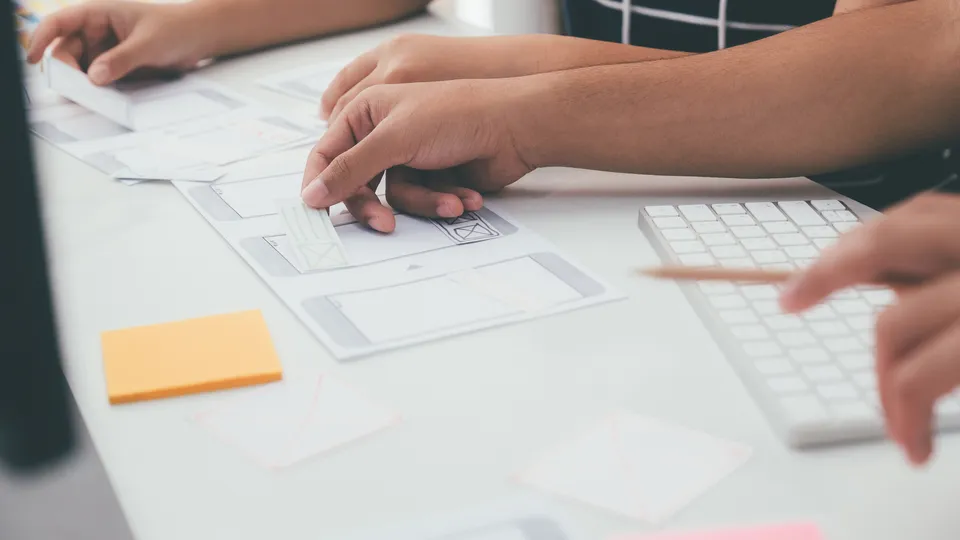Illustrative photo: Colleagues arranging paper interface layouts on a desk.