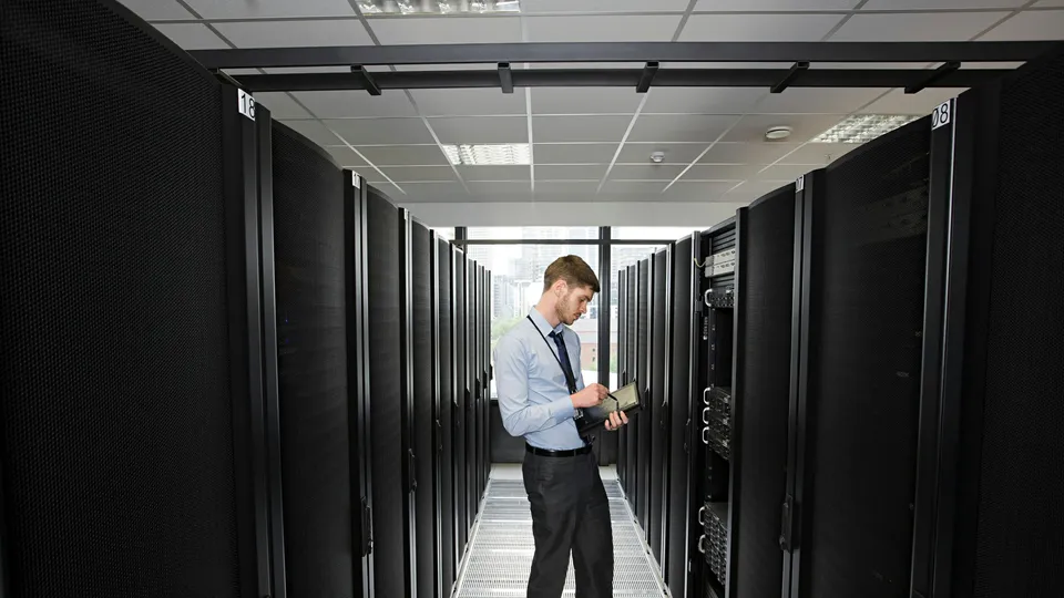 Illustrative photo: Technician with a tablet standing between rows of server racks.