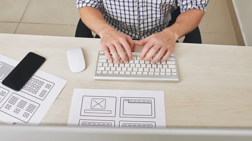 Illustrative photo: Designer working beside paper interface wireframes.