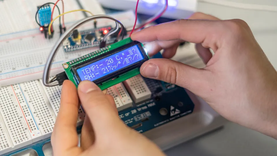 Illustrative photo: Hands working with a development board, breadboard and small display.
