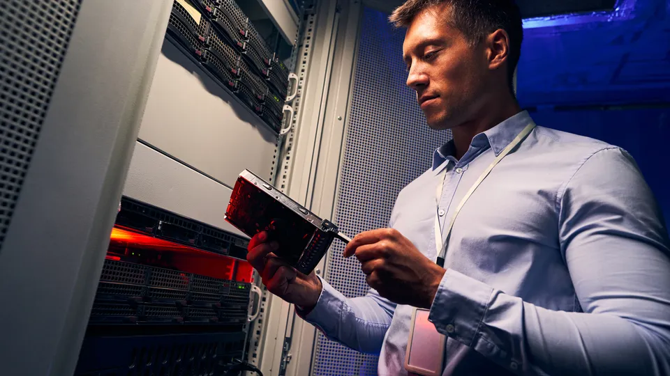 Illustrative photo: Technician using a tablet beside server racks.