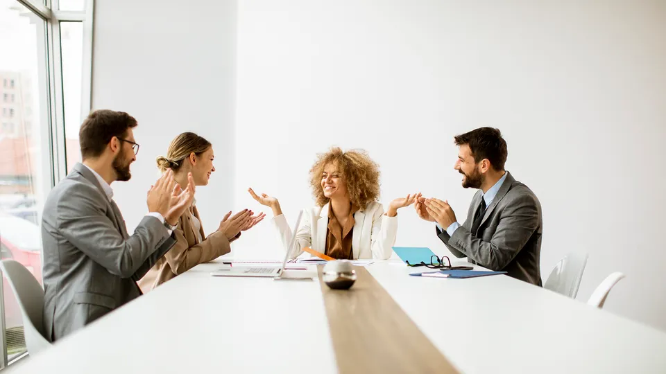 Illustrative photo: Colleagues gesturing during a discussion around a meeting table.