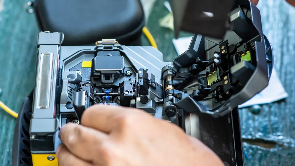 Illustrative photo: Hands operating a fiber optic fusion splicer.