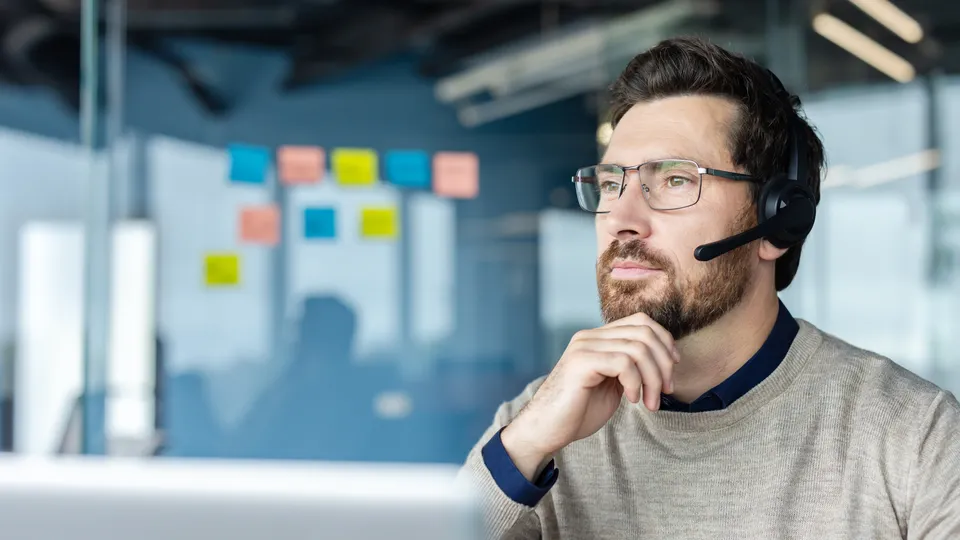 Illustrative photo: Man with a headset working at a laptop in an office.