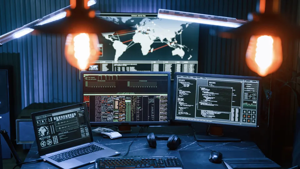 Illustrative photo: Workstation with multiple monitors displaying code and a world map.