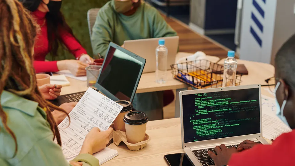 Illustrative photo: Developers discussing code around a table with laptops.