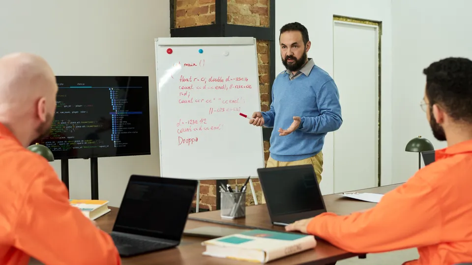Illustrative photo: Instructor teaching programming to people with laptops.