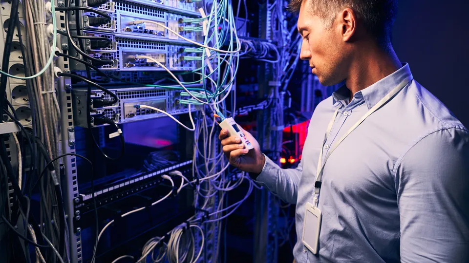 Illustrative photo: Technician inspecting network cables in a server rack.