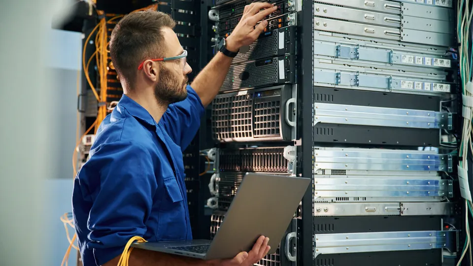 Illustrative photo: Technician using a laptop while working on rack equipment.