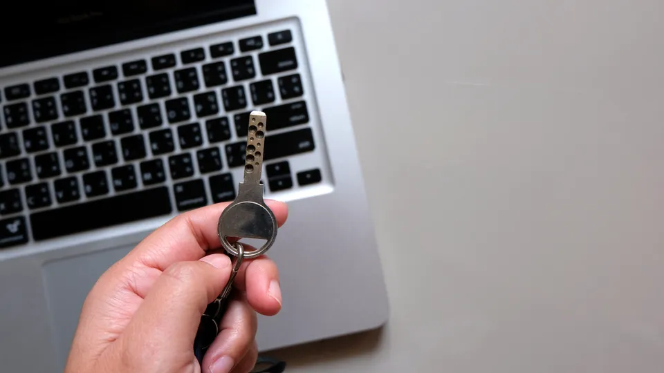 Illustrative photo: Hand holding a key beside a laptop.