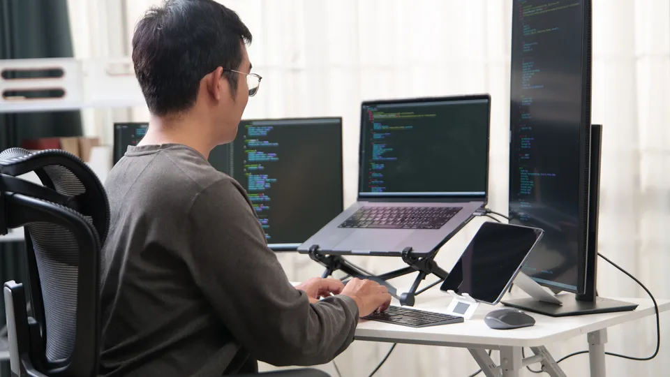 Illustrative photo: Developer working at a desk with several screens displaying code.