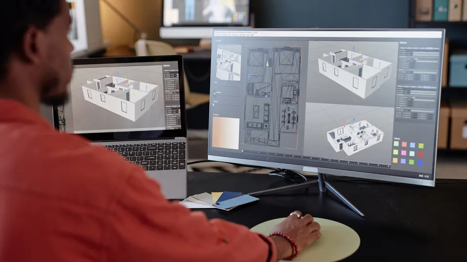 Illustrative photo: Designer reviewing three-dimensional building plans on two monitors.