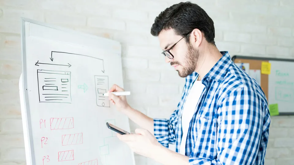 Illustrative photo: Man sketching interface layouts on a whiteboard.