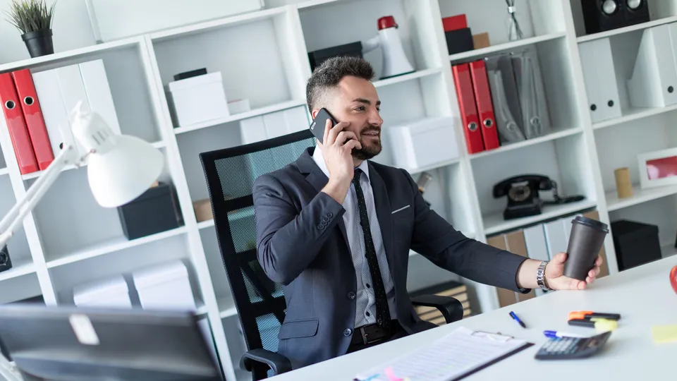 Illustrative photo: Business professional speaking on a phone at an office desk.