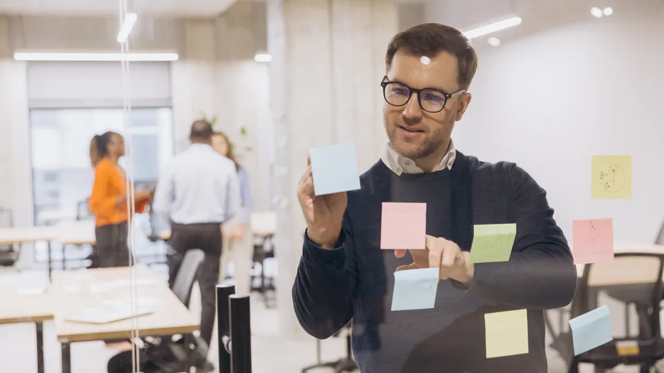 Illustrative photo: Man reviewing sticky notes on an office glass wall.
