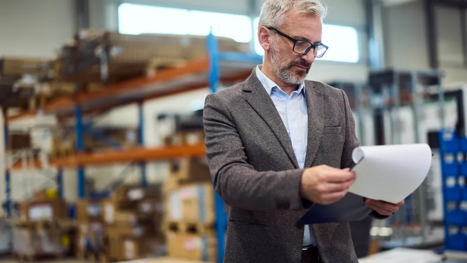 Illustrative photo: Man checking warehouse inventory with a document and scanner.