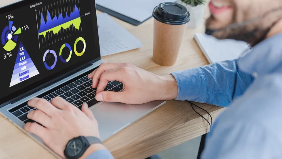 Illustrative photo: Hands using a laptop displaying charts and performance indicators.