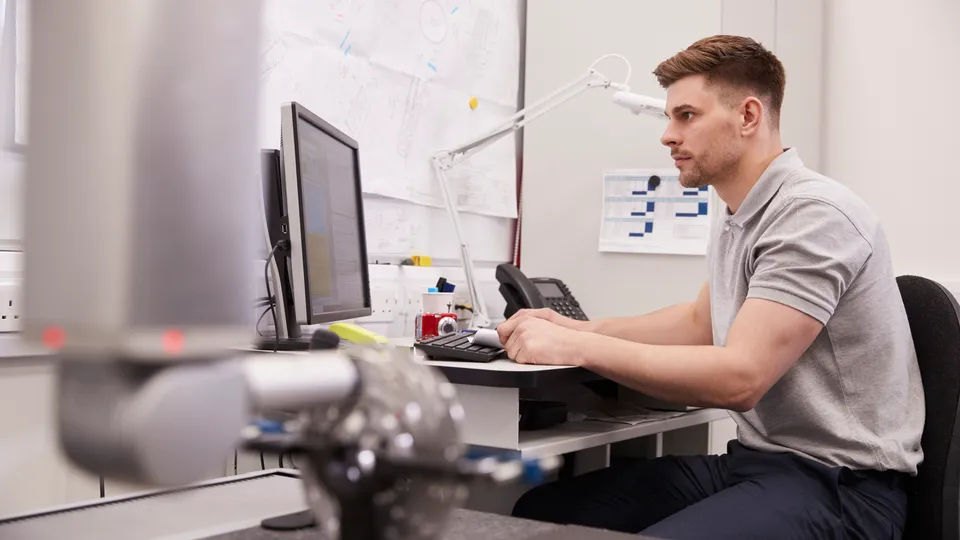 Illustrative photo: Man working at a computer beside mechanical equipment.