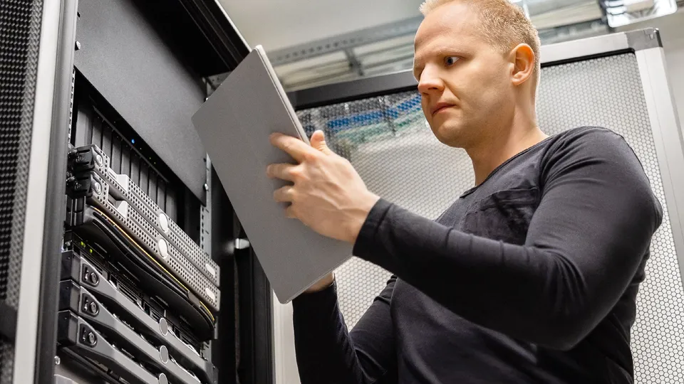 Illustrative photo: Technician inspecting equipment in a server rack.