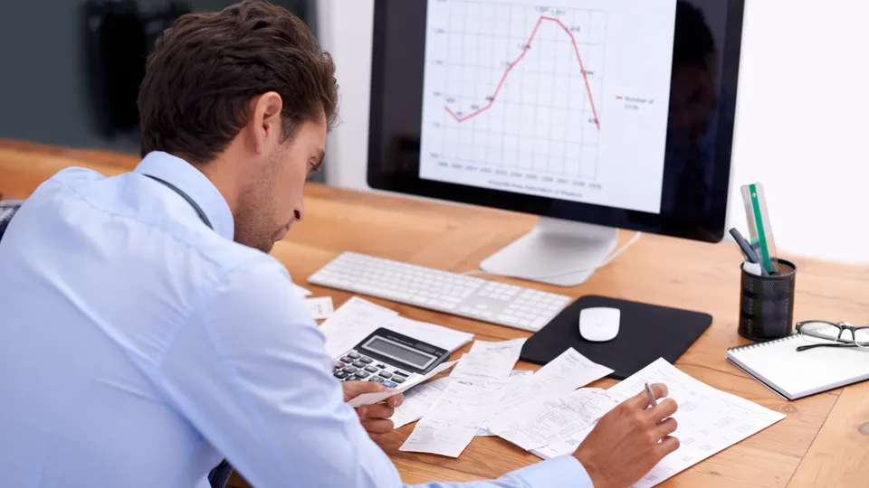 Illustrative photo: Man reviewing a chart on a monitor and notes on his desk.