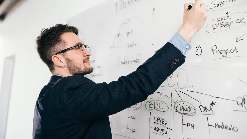 Illustrative photo: Man writing a business and project diagram on a whiteboard.