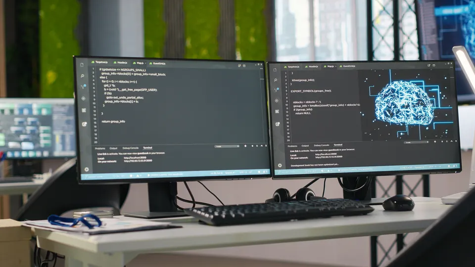 Illustrative photo: Desktop monitors displaying code and a digital neural-network illustration.