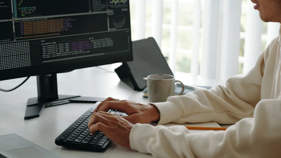 Illustrative photo: Person typing code at a desktop computer.