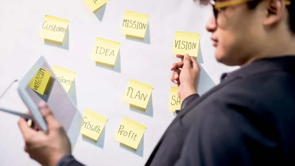 Illustrative photo: Person arranging notes about goals and plans on a whiteboard.